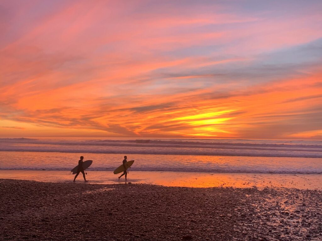 two people walking on the beach during sunset