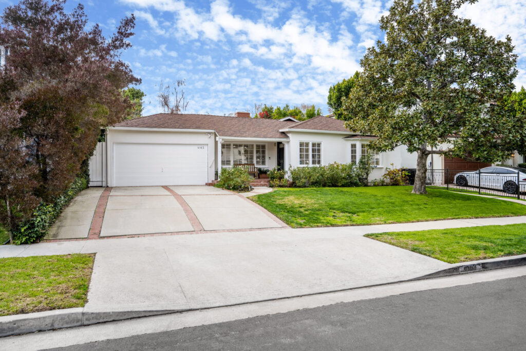 a white house with brown roof top and well maintained lawn and garage with wide drive way under the clear blue skies